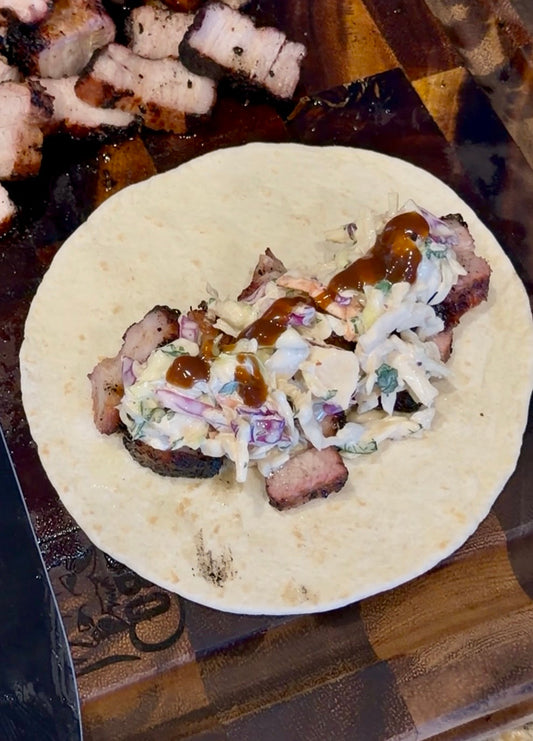 Filipino-style grilled pork belly taco topped with creamy Asian Bang Slaw, cilantro, and Asian Bang Sauce on a flour tortilla.