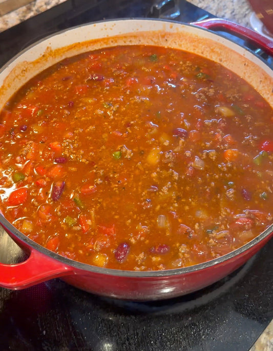 Homemade beef and sausage chili with kidney beans, tomatoes and diced peppers simmering in a red Dutch oven.
