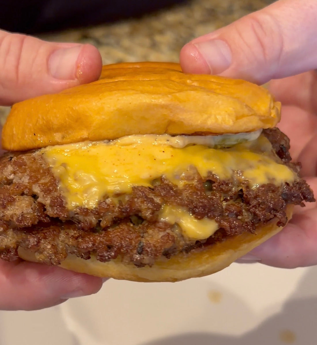 Double smashburger with crispy beef patties, melted American cheese and burger sauce on a toasted golden bun, held in two hands.