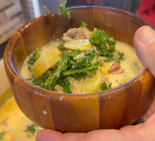 Creamy Zuppa Toscana soup with Italian sausage, sliced gold potatoes, bacon and kale in a wooden bowl held in two hands.